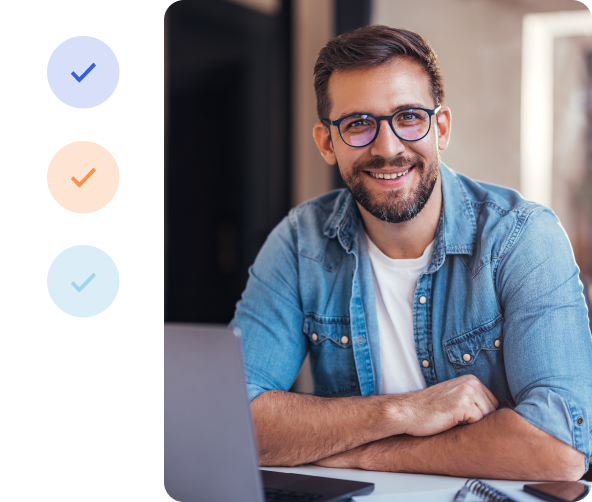 A casually dressed man smiles seated in front of a laptop