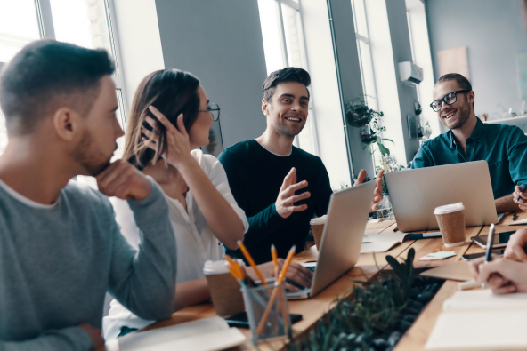 Colleagues converse while seated at a modern conference table with laptops