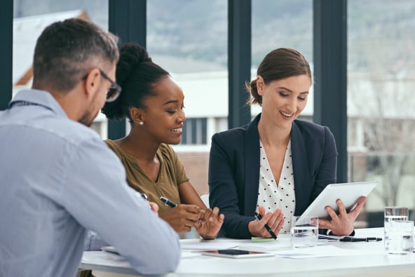 Professional people meet cordially around a conference table and look at a tablet