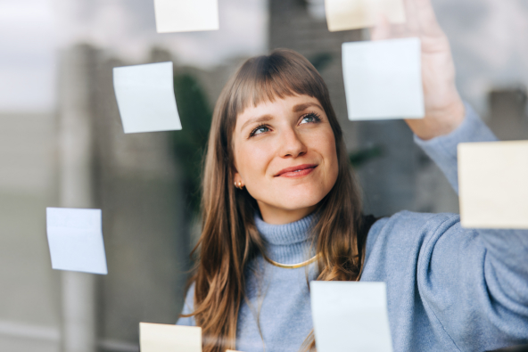 A person smiling places sticky notes on a clear glass wall