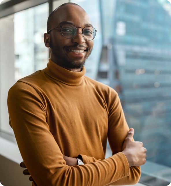 A young person in an orange turtleneck with arms crossed and smiling